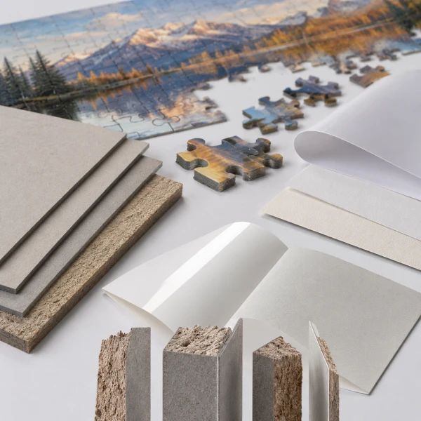 Raw materials used in puzzle manufacturing including grey board, chipboard, coated paper, and laminated puzzle components